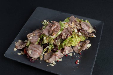 Tütsülenmiş ördek etli salata, siyah seramik tabakta badem taneli tatlı ve ekşi sos.