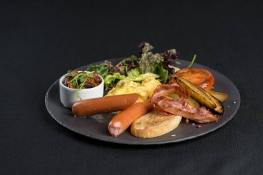 Geleneksel İngiliz kahvaltısı beyaz tabakta. Sosis, fasulye, yumurta, ekmek ve salata. Siyah masa örtüsü