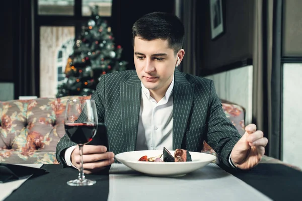 Молодий і привабливий чоловік використовує свій телефон під час їжі телятини в попелі з овочами на грилі в критому ресторані — стокове фото