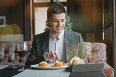 Genç ve çekici bir adam telefonunu kullanırken leziz yumurtalar hafif tuzlu somon ve sos ile birlikte kapalı bir restoranda.