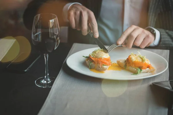 Молодой и привлекательный мужчина пользуется телефоном, в то время как вкусные яйца Бенедикт с слегка соленым лосося и соусом в закрытом ресторане — стоковое фото