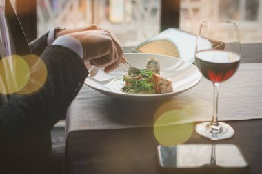 Genç ve çekici bir adam tabletini içerideki bir restoranda hindi fileto ve bezelye püresi yerken kullanıyor.