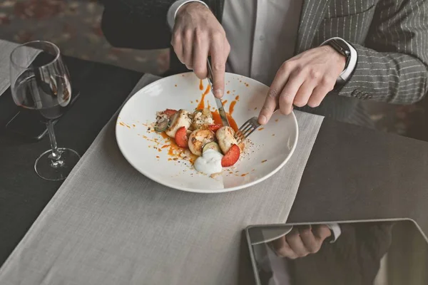 Молодой привлекательный мужчина ест блинчики со сметаной и миндальными хлопьями и апельсиновым соусом из облепихи в закрытом ресторане — стоковое фото