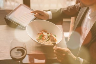 Genç ve çekici bir adam tabletini içerideki bir restoranda hindi fileto ve bezelye püresi yerken kullanıyor.