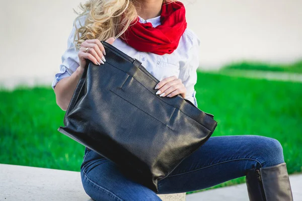 Модная женщина позирует на улице с черной кожаной сумкой. Модель в модном синем джинсе, шарфе — стоковое фото