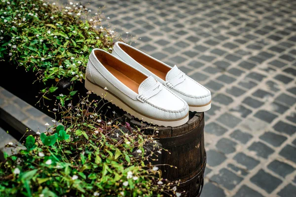 Mocasines de cuero blanco. Foto en la calle junto a las flores. Mocasines blancos de moda. Zapatos de cuero para mujer de moda. — Foto de Stock