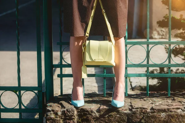 Fashionable young woman in brown dress and blue high heel shoes with yellow handbag in hand on the city streets. Fashion. — Stock Photo, Image