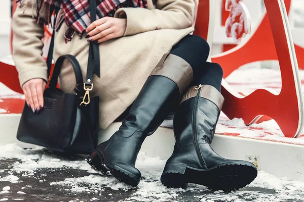 Stílusos nő ül a járdán egy kabát, városi utcai stílus, téli divat trend, lábak közelről, kiegészítők, fekete csizma és táska — Stock Fotó