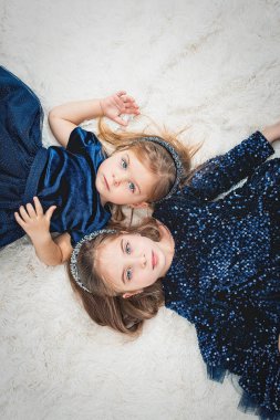 Mavi gözlü iki tatlı kız kardeş sırt üstü uzanmış sahte kürklü mavi elbiselerle.