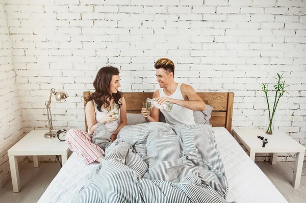 Joyeux couple youmg en pyjama avec des verres d'eau sur le lit à la maison — Photo