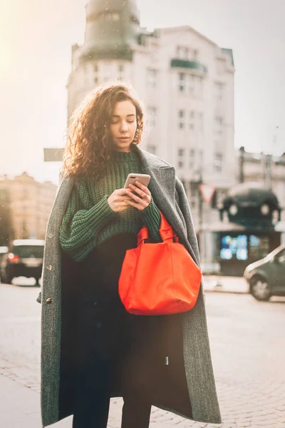 Una mujer en la calle usa un teléfono móvil. compras en línea. uso de aplicaciones móviles. Clima lluvioso. Grano de película. Ruido — Foto de Stock