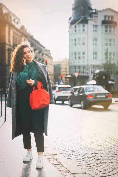 Una mujer en la calle usa un teléfono móvil. compras en línea. uso de aplicaciones móviles. paisaje urbano sobre un fondo. Grano de película. Ruido — Foto de Stock