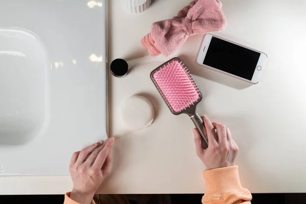 Bad-Accessoires von oben, Zahnbürste in der Nähe von Haarbürste, Schleife, Handy und Gesichtsschwamm auf weißer Oberfläche — Stockfoto