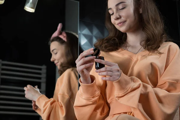 Frau hält ein offenes Glas Creme und gibt eine kleine Menge des Produkts auf ihre Hand. Konzept der Hautpflege, Prüfung und Auswahl hochwertiger Natur- und Biokosmetik. — Stockfoto