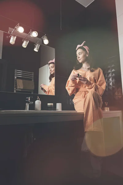 Portret van een mooie jonge vrouw die zich klaarmaakt in de badkamer. hydraterende crème. vrouwelijke cosmetica, spiegel gezicht reflectie. — Stockfoto