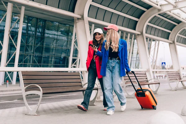 Duas meninas felizes usando smartphone verificando voo ou check-in on-line no aeroporto juntos, com bagagem. Viagens aéreas, férias de verão — Fotografia de Stock