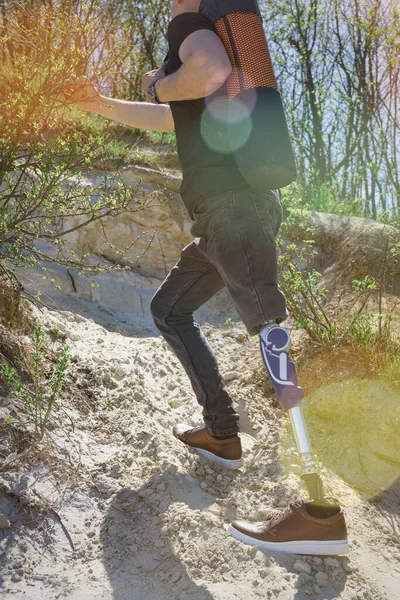 Um homem numa perna protética viaja pelas montanhas. Vestido com jeans pretos e uma camiseta, ele carregando tapete — Fotografia de Stock