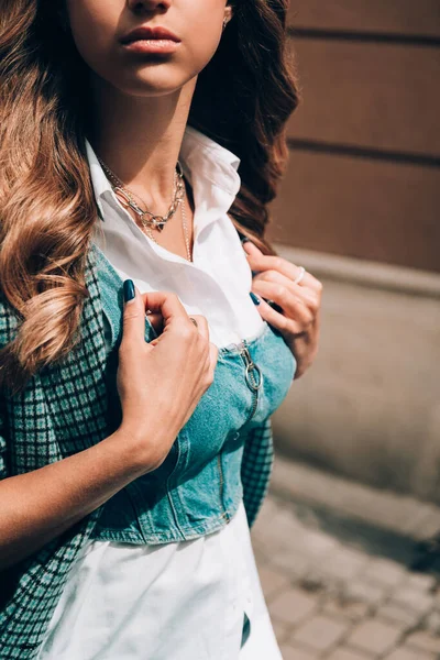 금발의 젊은 여자가 하얀 블라우스와 데님 윗옷을 입고 이렇게 체크무늬 코트 포즈를 하는 것은. — 스톡 사진