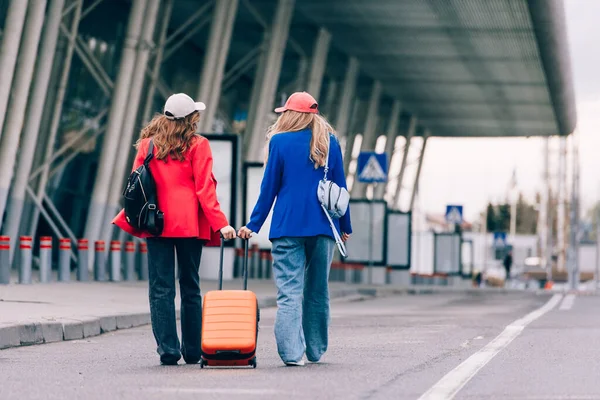 Две счастливые девушки, гуляющие возле аэропорта, с рюкзаками. Авиабилеты, летние каникулы — стоковое фото