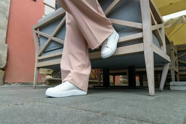 Stijlvolle vrouw in de mode witte sneakers schoenen en beige broek loopt rond in de stad. — Stockfoto
