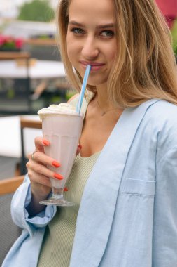 Bir kadının eli, tazeleyici bir kokteyli tüple bardakta tutar..