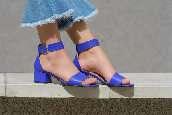 Piernas de mujer en vaqueros azules y sandalias en la calle de la ciudad. Traje casual elegante de moda. Detalles del look diario de verano. — Foto de Stock