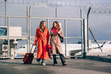 Havaalanının yakınında bavullarıyla yürüyen iki mutlu kız. Hava yolculuğu, yaz tatili.