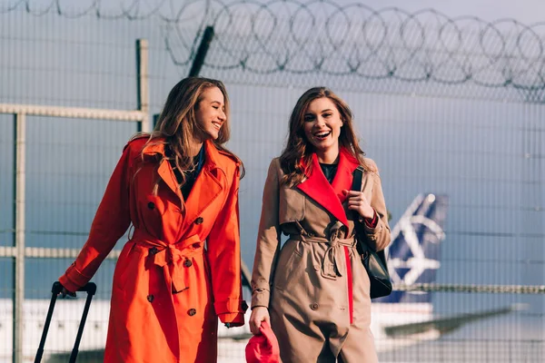 Dos chicas felices caminando cerca del aeropuerto, con equipaje. Viajes aéreos, vacaciones de verano — Foto de Stock