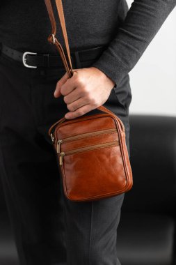 Beyaz bir stüdyo arka planına karşı konyak derisi dikey kurye çantası giyen, yaka yaka yakalı bir erkek model ve özel dikey pantolon giyiyor.