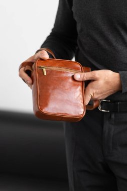 Beyaz bir stüdyo arka planına karşı konyak derisi dikey kurye çantası giyen, yaka yaka yakalı bir erkek model ve özel dikey pantolon giyiyor.