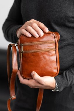 Beyaz bir stüdyo arka planına karşı konyak derisi dikey kurye çantası giyen, yaka yaka yakalı bir erkek model ve özel dikey pantolon giyiyor.