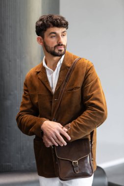 Kahverengi kadife ceketli, beyaz gömlekli şık bir adamın portresi. Stüdyoda bir konyak deri bir kurye çantası tutuyor.