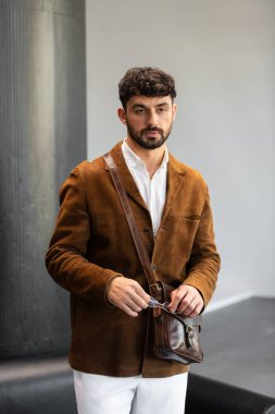 Kahverengi kadife ceketli, beyaz gömlekli şık bir adamın portresi. Stüdyoda bir konyak deri bir kurye çantası tutuyor.