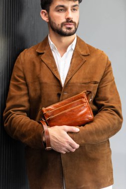 Kahverengi süet ceketli, deri bileklik çantası tutan şık bir adamın fotoğrafını çek..