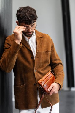 Kahverengi süet ceketli, deri bileklik çantası tutan şık bir adamın fotoğrafını çek..