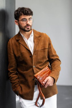 Kahverengi süet ceketli, deri bileklik çantası tutan şık bir adamın fotoğrafını çek..