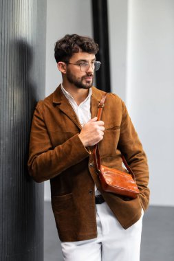 Kahverengi süet ceketli, deri bileklik çantası tutan şık bir adamın fotoğrafını çek..