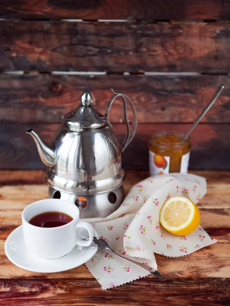 Taza de té negro en una tetera con un limón y mermelada en una madera oscura —  Fotos de Stock