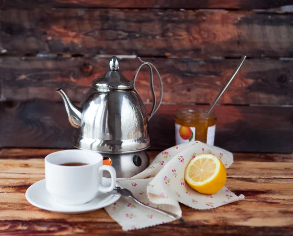 Secangkir teh hitam dalam teko teh dengan lemon dan selai pada kayu gelap — Stok Foto