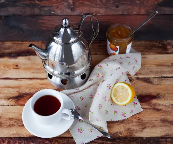 Secangkir teh hitam dalam teko teh dengan lemon dan selai pada kayu gelap — Stok Foto