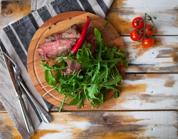 Steak de viande coupé savoureux avec des verts et de la roquette sur une assiette en bois a — Photo