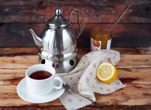 Taza de té negro en una tetera con un limón y mermelada en una madera oscura —  Fotos de Stock