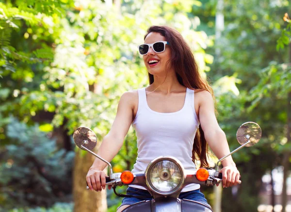 Die glückliche junge Frau auf dem Motorroller im Stadtpark im Sommer — Stockfoto