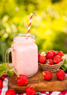 Çilek güler yüzlü veya milkshake kavanoza doğal arka planda, s