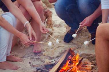 Daire marshmal ile plajda kum üzerinde oturan arkadaşlar