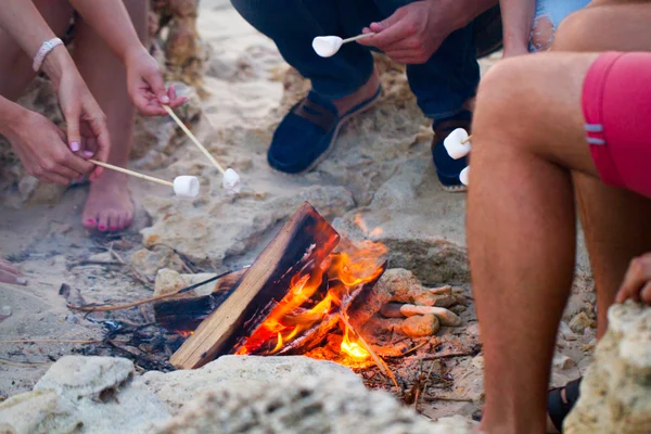Freunde sitzen am Strand im Kreis mit Marshmallow auf dem Sand — Stockfoto