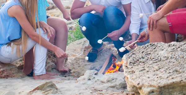 Freunde sitzen am Strand im Kreis mit Marshmallow auf dem Sand — Stockfoto