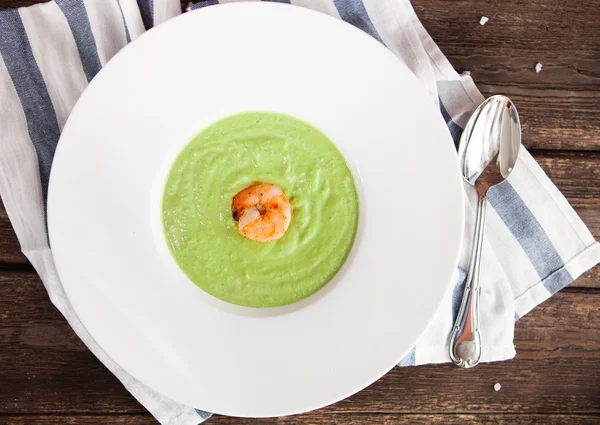 Green Cream of asparagus soup with shrimp in a white bowl on a r — Stock Photo, Image