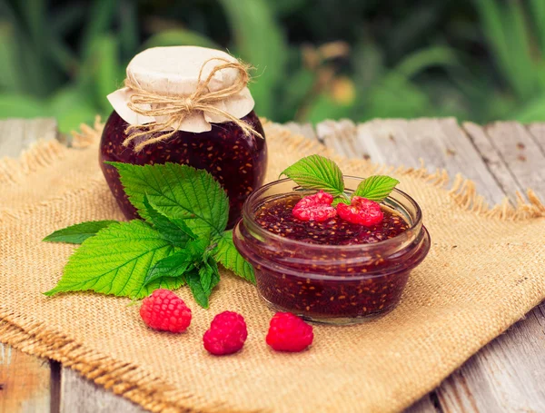 Fresh raspberries and jam on wooden table — Stockfoto