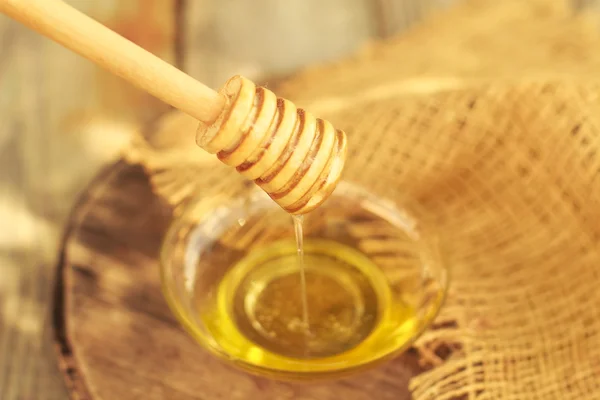 Honey dripping from a wooden honey dipper on blurred background — Stock Photo, Image